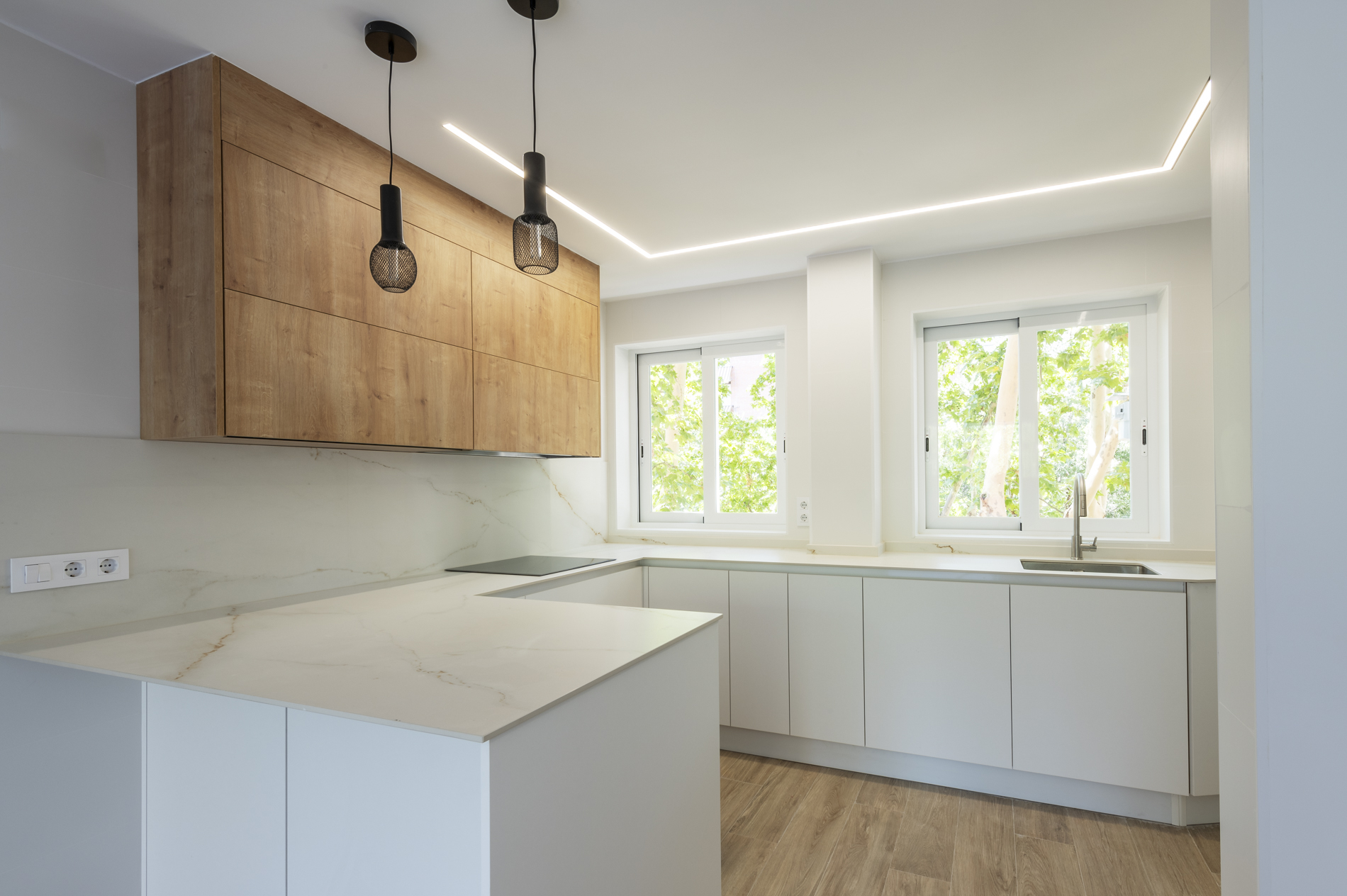 Cocina blanca muy luminosa con mueble superior de madera y lámparas colgantes