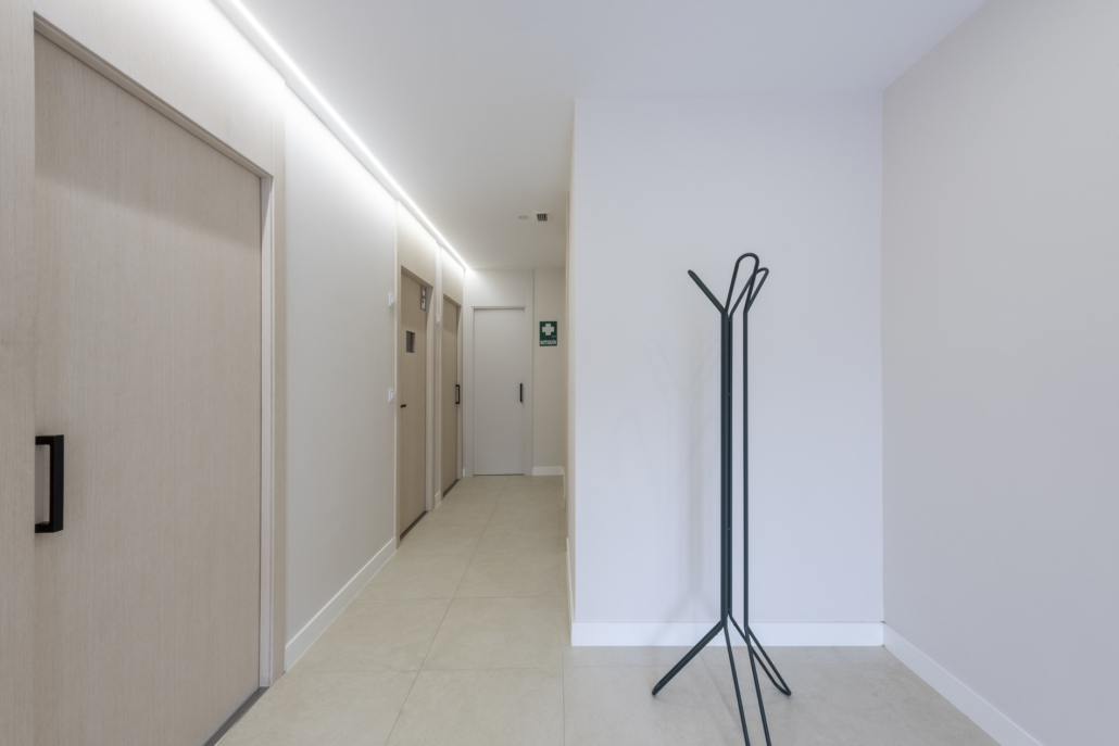 Pasillo de un dentista en tonos claros iluminado con una tira led en el techo.